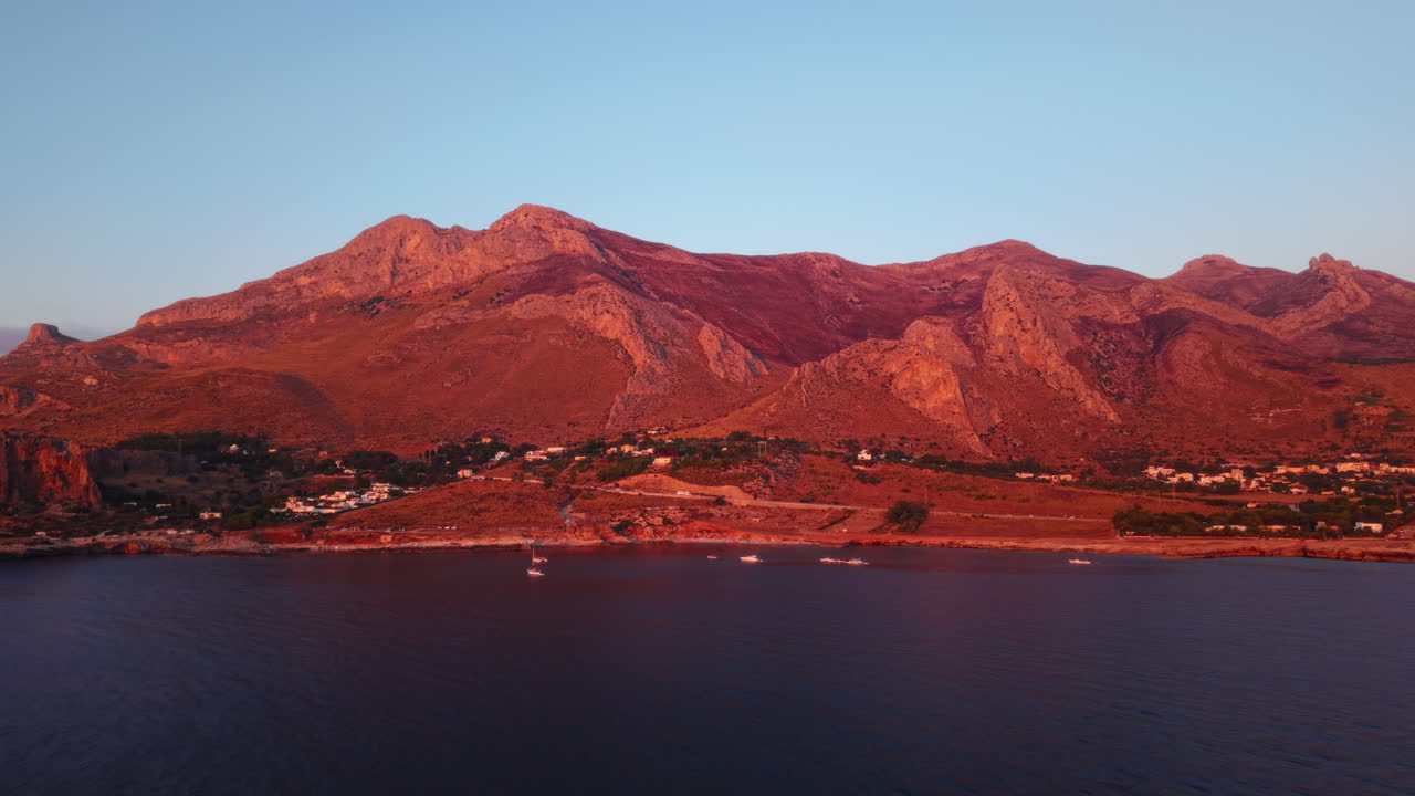 Sunset view of Sicilian coastline with red-hued mountains and calm sea