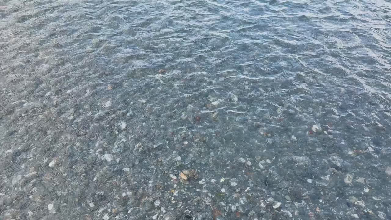 Clear lake water with small ripples flows over rocky shoreline, captured in soft natural daylight