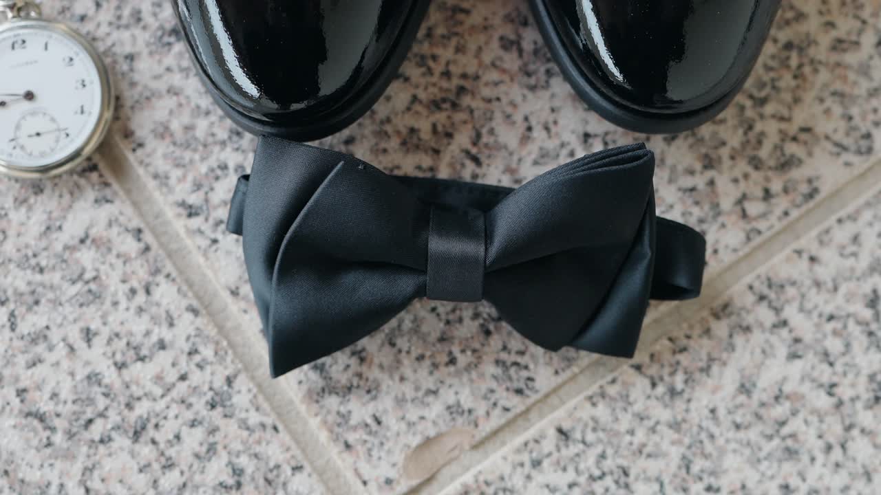 black bow tie with polished shoes and pocket watch on stone floor