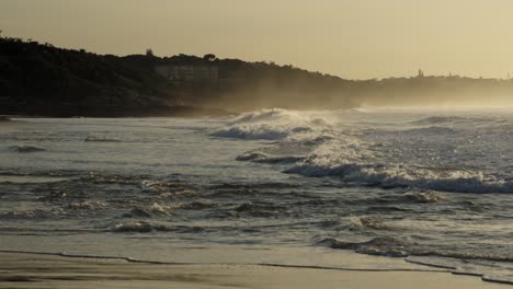 a panning shot follows waves racing along the shore, gradually revealing the misty shoreline in the distance.