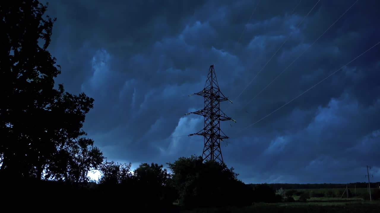 Stormy weather in nature. Dark clouds moving on the sky over the tower of high voltage electricity. Strong wind shaking trees in the evening.