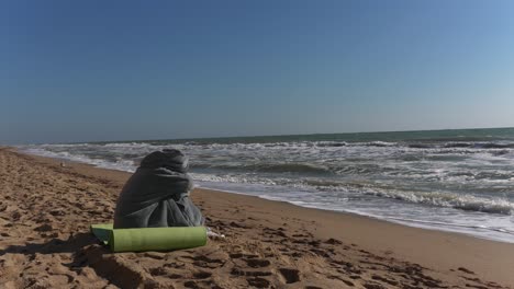 person wrapped in blanket, sitting on a beach