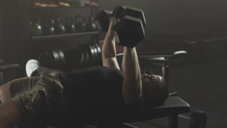 man performing dumbbell bench press exercise in gym