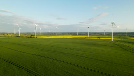 Aerial---drone-desanding-over-windmills-farm-park-and-agricultural-green-fields-on-a-sunny-cloudy-day,-copy-space-template