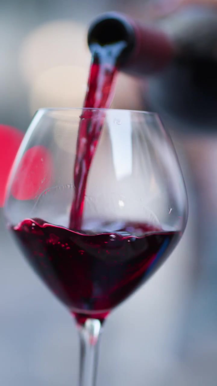 Vino rosso che scorre in un elegante bicchiere, luci bokeh serali, ambientazione esterna, profondità di campo ridotta.