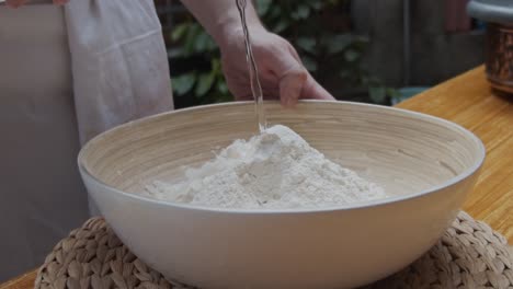 el chef vierte agua sobre la masa de pizza en un plato hondo