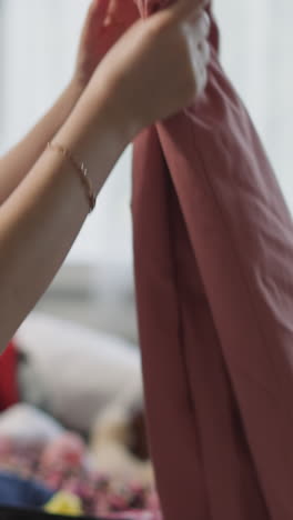 woman folds pink trousers to put into suitcase in living room closeup. lady gathers clothes for family vacation in apartment. preparation for travel