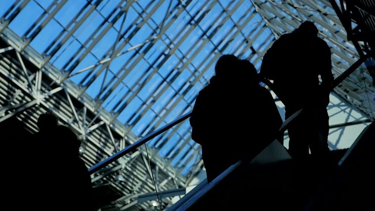 People silhouettes on escalator moving in business center with large windows