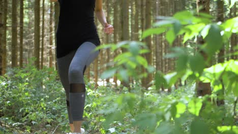 una mujer rubia y en forma que corre por el bosque pasa junto a la cámara mientras se mueve a través de su camino en un ángulo bajo