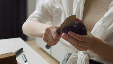 close up of a woman hands cutting avocado and scooping the flesh out using a spoon