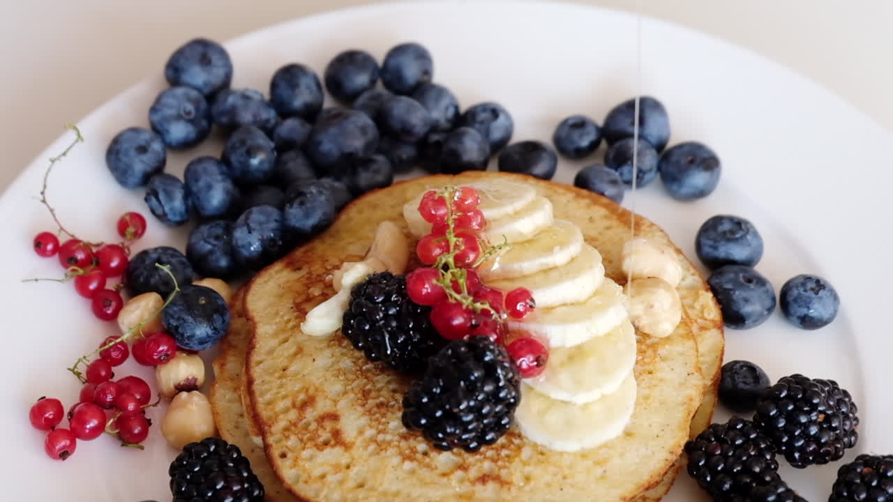 Woman pouring honey over a stash of pancakes with different fruit