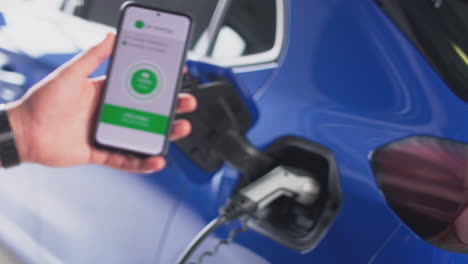 hombre cargando un coche eléctrico con un cable usando una aplicación en el teléfono para monitorear el nivel de carga de la batería