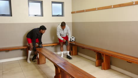 in locker room, two soccer players talking and holding soccer ball and shoes