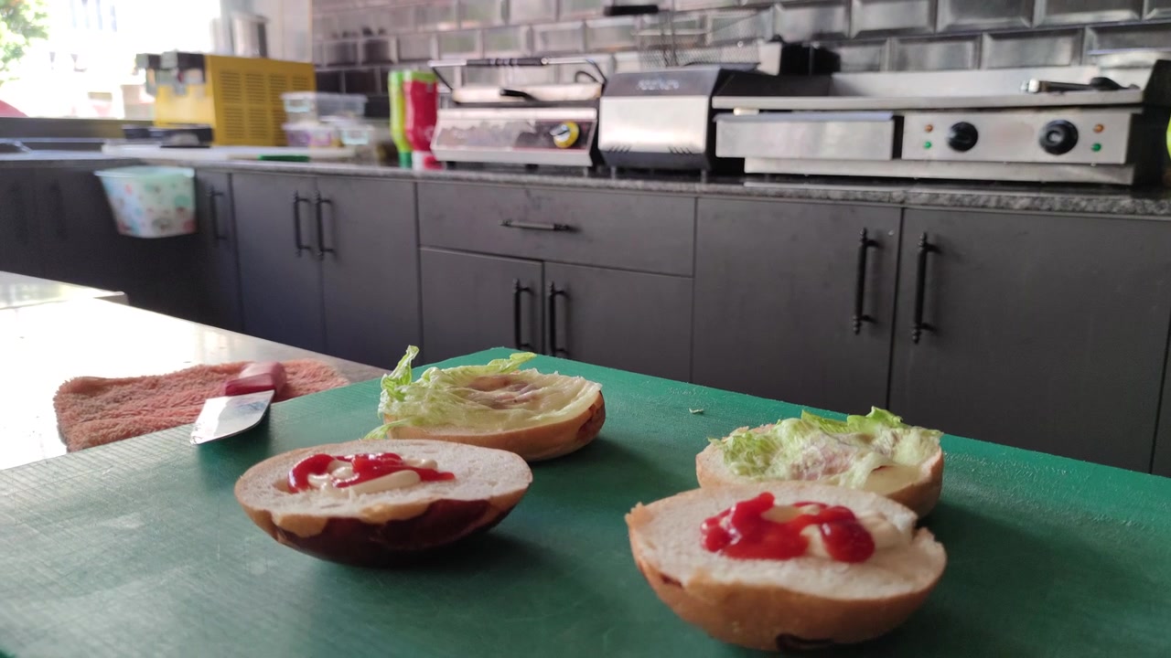 Forbereder burgerboller med salat og ketchup i et storkøkken.