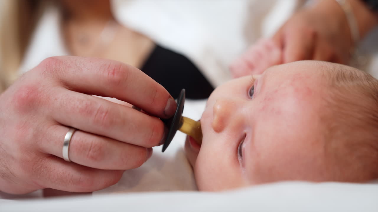 Dad's hand giving a pacifier to a newborn. Baby takes a pacifier and starts to sick it. Close up.