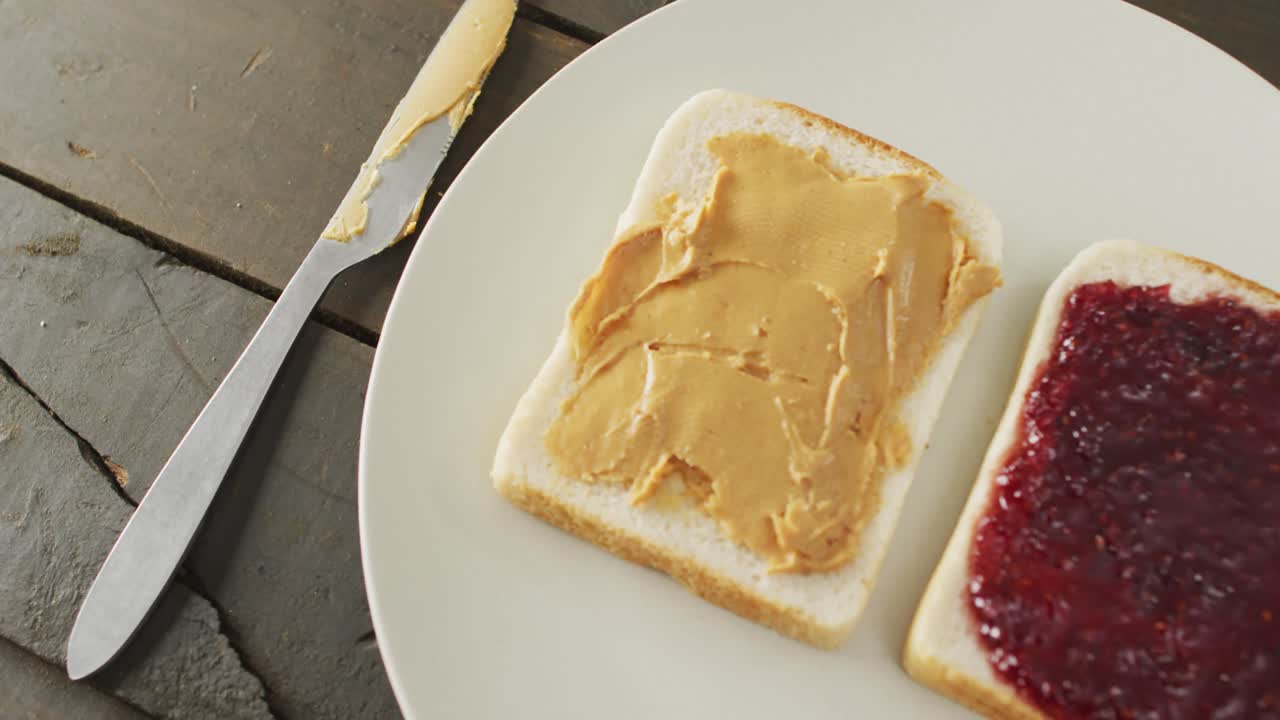 Close up view of peanut butter and jelly sandwich in a plate with butter knife on wooden surface