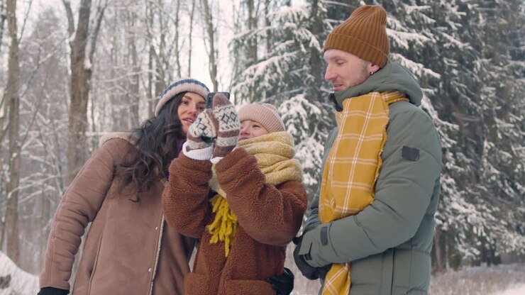 Parents et fille vêtus de vêtements d'hiver, prenant des photos du paysage enneigé.