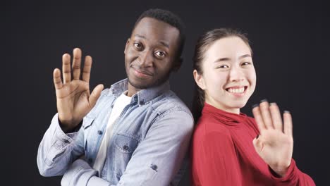 African-man-and-Asian-woman-looking-at-camera-and-waving-in-happy-relationship.