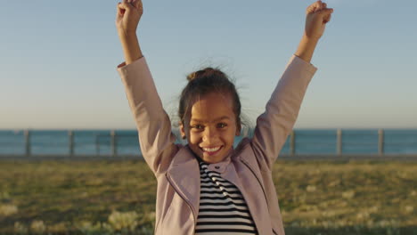 portrait of little mixed race girl happy cheerful celebrating arms raised dancing excited enjoying seaside park