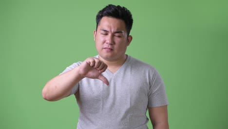 young handsome overweight asian man against green background