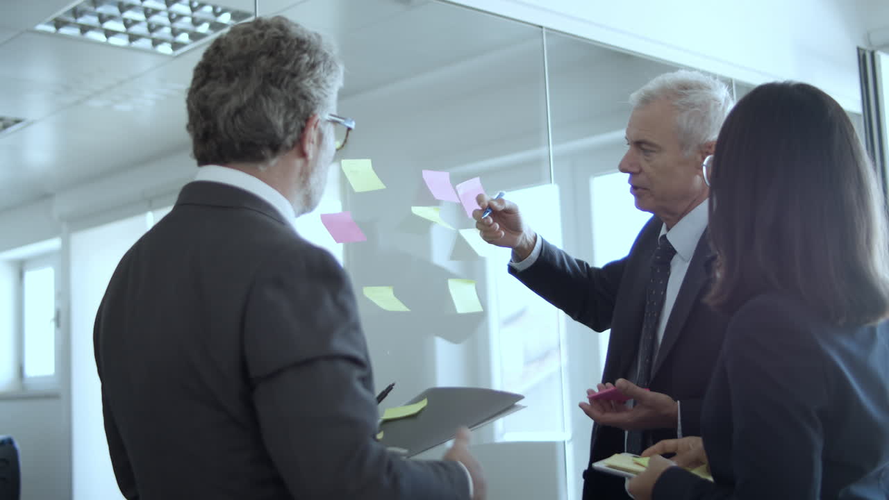 Business people of different ages sticking paper notes and writing on them at the office