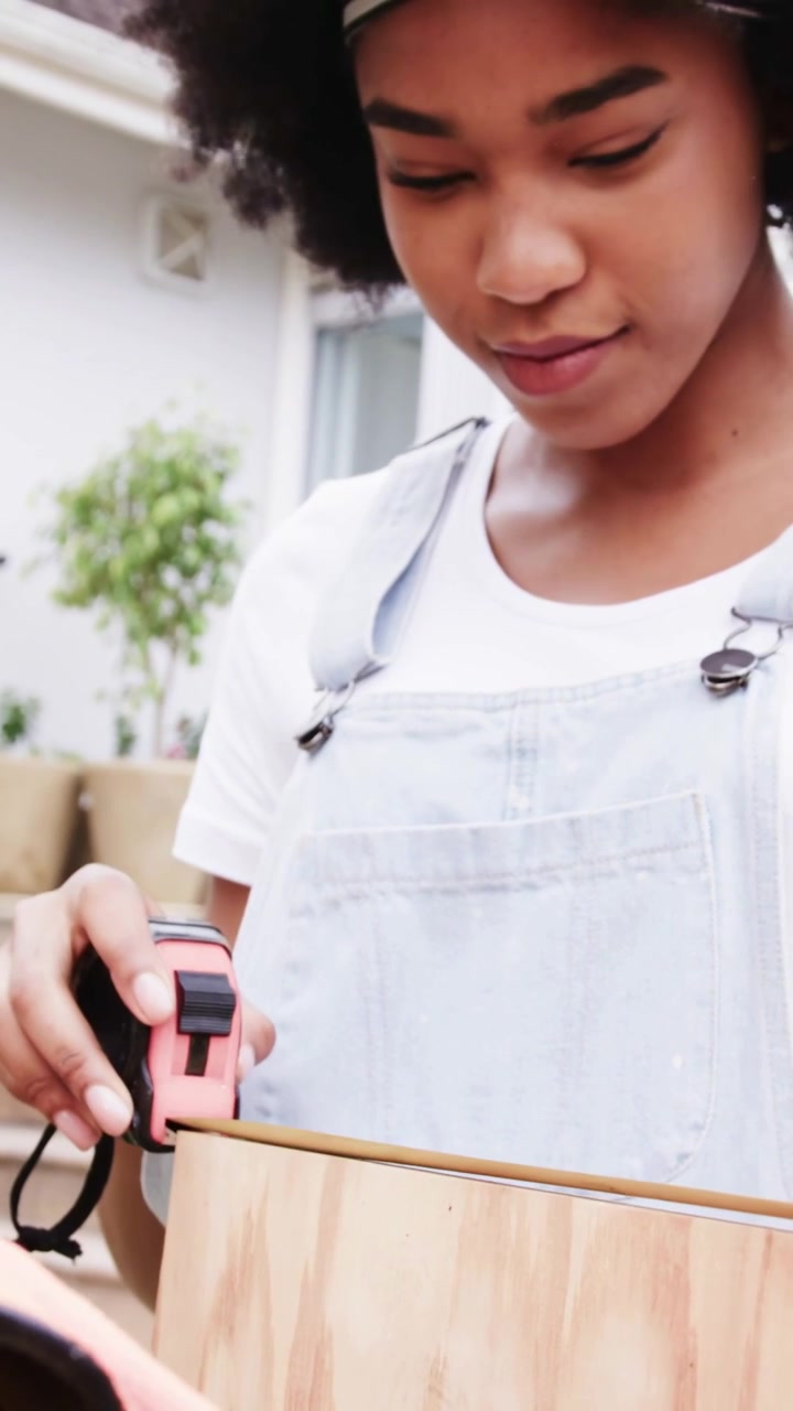 Vertical video: Pulling tape woman in overalls aligning pink tape on patio for board cut
