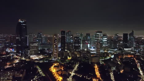 Aérea-De-Noche:-El-Distrito-Financiero-De-París-Brilla,-Un-Faro-Del-Comercio-Moderno.