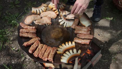 Person-turns-Szalonna,-or-pork-fat,-cooking-over-fire-with-other-Romanian-foods