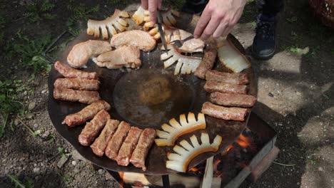 person turns szalonna, or pork fat, cooking over fire with other romanian foods