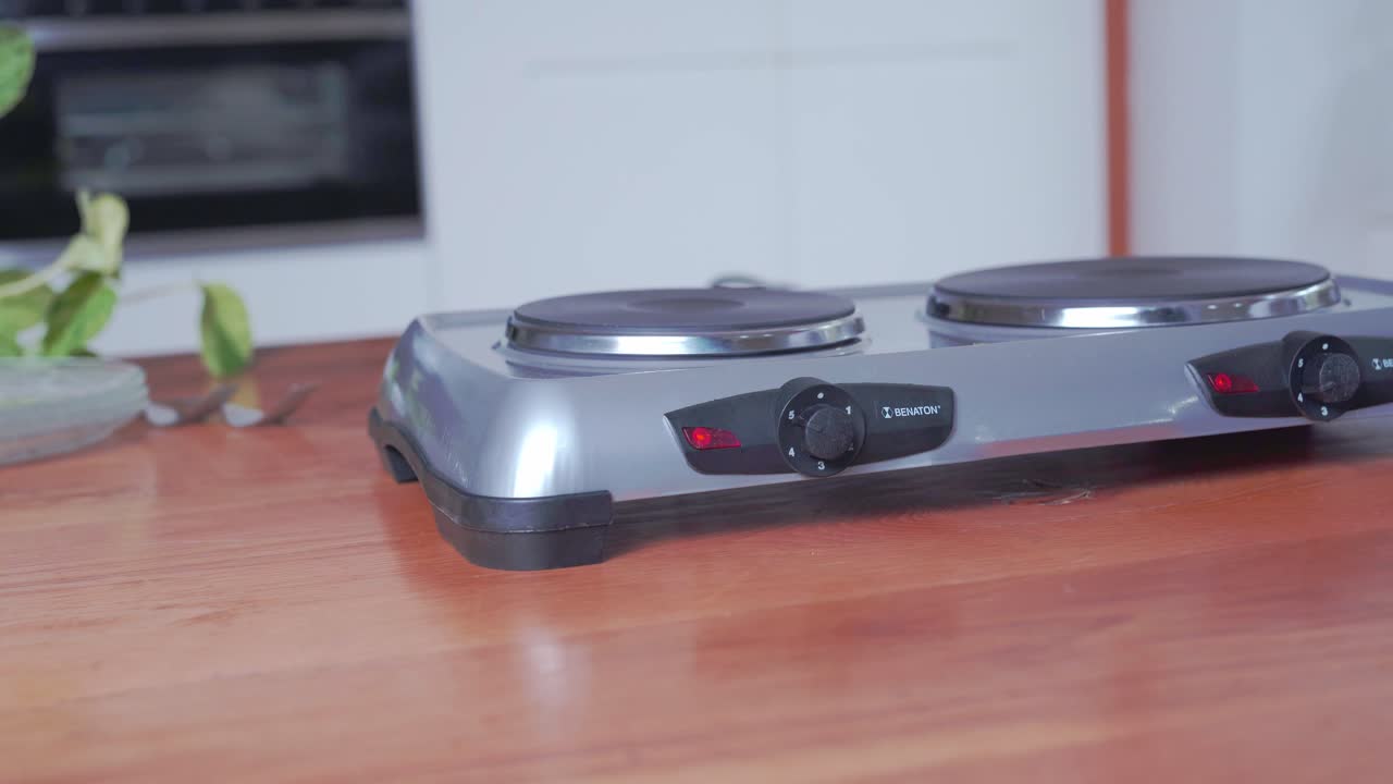 Draagbaar klein elektrisch kooktoestel op aanrecht, hand past warmte-instelling aan