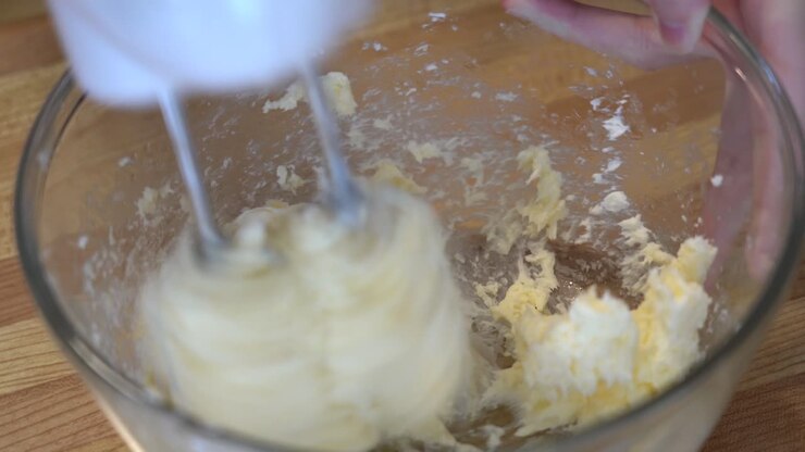 Mescolare burro e altri ingredienti in una ciotola con uno sbattitore elettrico a casa.