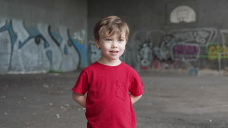 a young little boy is having fun and making expressions in front of camera in a red t-shirt, hands behind back