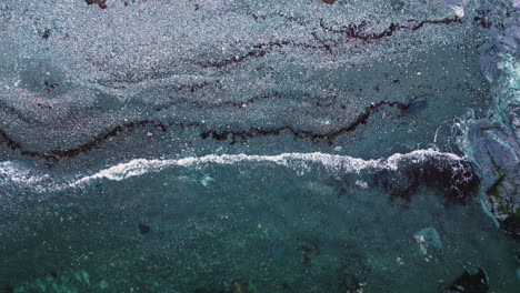 clear ocean wave whitewash water crashes on grey sandy shoreline, drone top down