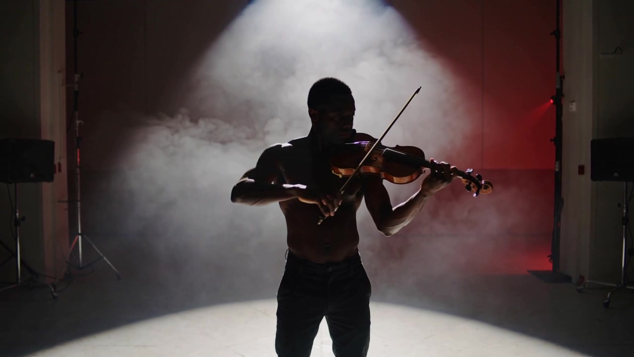 Violinist med bar overkrop løfter buen og spiller violin på en studiescene med tåget spotlight