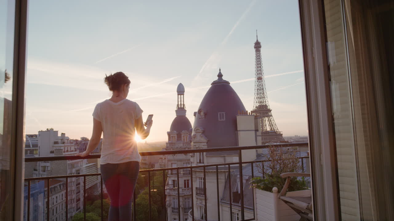 donna felice che usa lo smartphone che scatta foto che si gode di condividere l'esperienza delle vacanze estive a parigi che fotografa la bellissima vista del tramonto della torre eiffel sul balcone