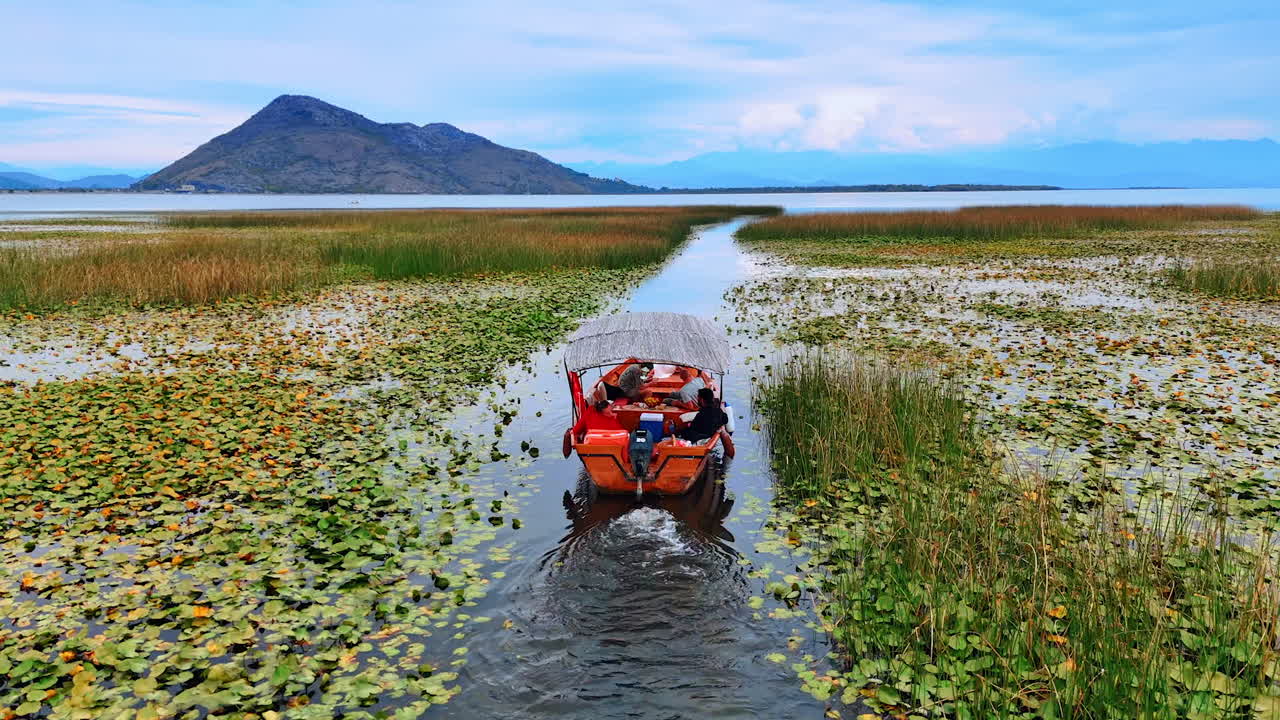 Ulcinj, Montenegro, 14 agosto 2025: barca che si avvicina a un'ampia vista sul lago. Una barca naviga attraverso l'acqua limpida del lago verso una vista distante sulle montagne.