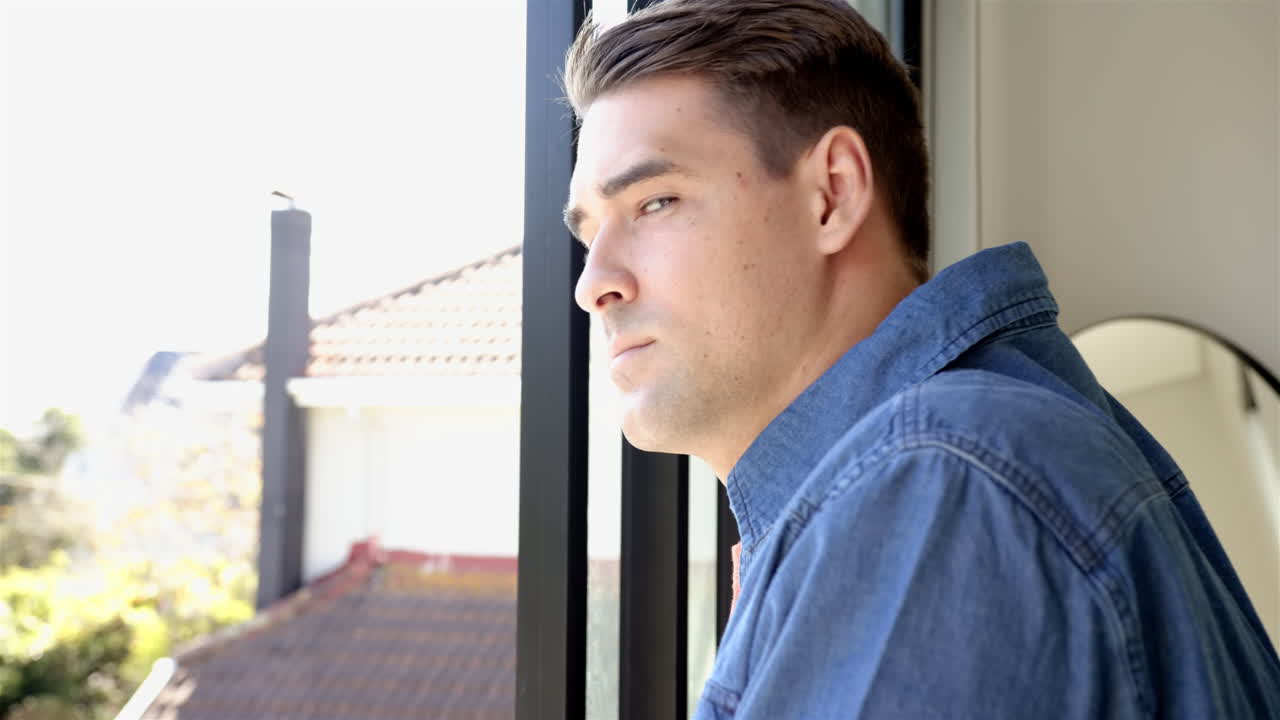 Smiling man in denim shirt looking out window, enjoying view, at home
