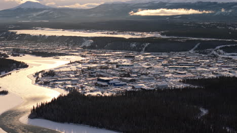 gorgeous sunset aerial shot over whitehorse, yukon, with snow-covered landscapes and the glistening yukon river reflecting the golden light.