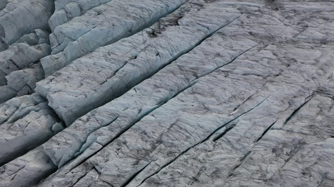 toma de dron mirando hacia abajo y moviéndose hacia la derecha, revelando más patrones, líneas y grietas interesantes y hermosos del glaciar de hielo.