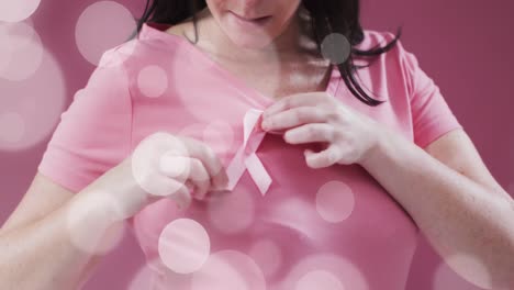 animation of light spots over caucasian woman with pink ribbon on pink background