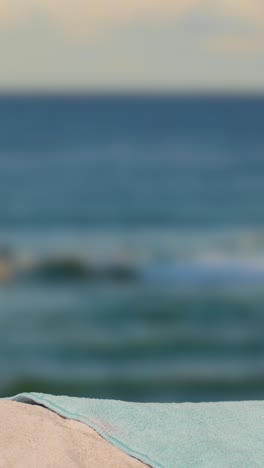 Vertical-Video-Summer-Holiday-Concept-Of-Hand-Picking-Up-Sun-Hat-Sunglasses-Beach-Towel-On-Sand-Against-Sea