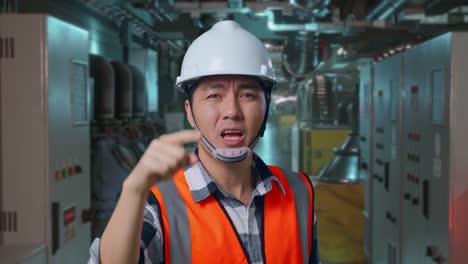 close up of angry asian male engineer with safety helmet shouting at someone while standing in engine control room, work of electrical generators