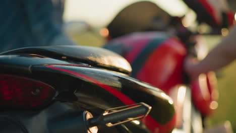 close-up shot of a red and black motorcycle being cleaned by two people, the bike s back seat and tail light are in focus, while one person can be seen blurred in the background