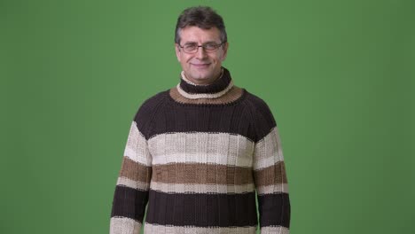 mature handsome man wearing turtleneck sweater against green background