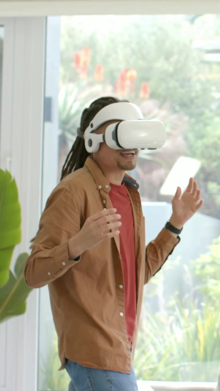 Video verticale: Uomo in soggiorno che indossa un visore VR bianco, ne regola la calzata e testa contenuti VR.