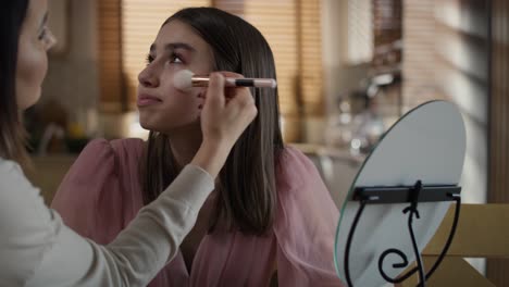 caucasian woman teaching daughter how to do make up to the mirror