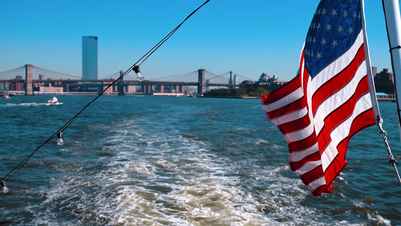 Bandiera americana sull'albero della barca che naviga sull'East River. Il famoso Manhattan Bridge e il Brooklyn Bridge sullo sfondo