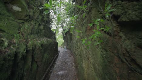 Woman-walking-through-rock-cut-out-levada-waterway-in-Madeira,-travel-trip