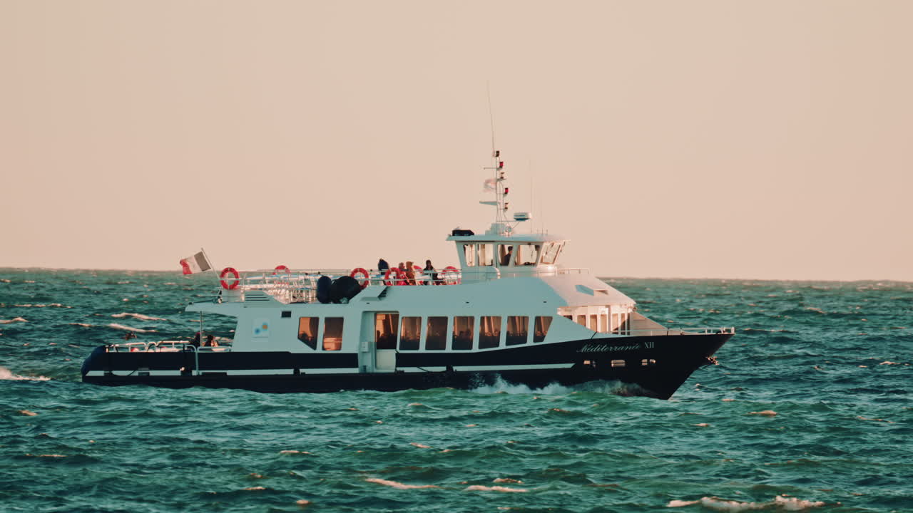 Cannes, France - November 18, 2025: A side view of a passenger ferry named Mediterranee XII, sailing over wavy waters under warm sunset light