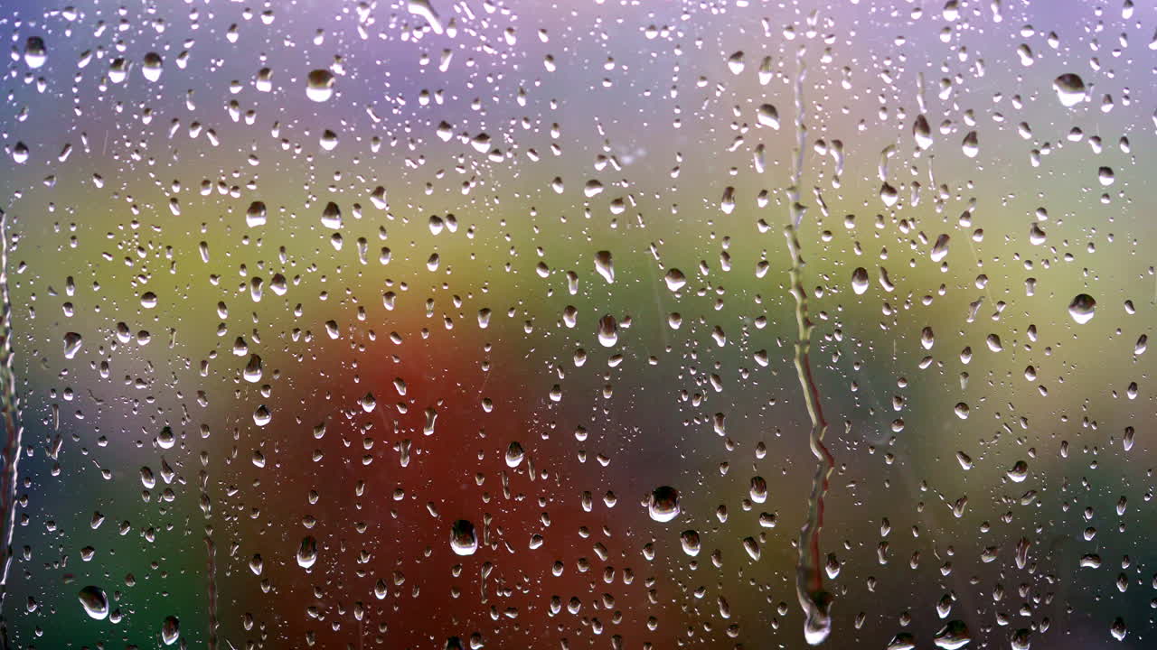 Water droplets on glass surface. Rainy weather. Raindrops on window. Water drops flowing down the window on blur colorful background. Close-up.
